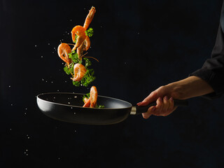Sea food. King prawns and parsley in a pan in a frozen flight in the hand of a professional chef. Isolated on black background. Asian cuisine for gourmets. Restaurant, hotel, banquet, recipe book. - 499018252