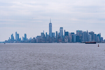 A tugboat pushing a barge in New York Harbor with the Manhattan Skyline in the background.   New York City, New York, USA