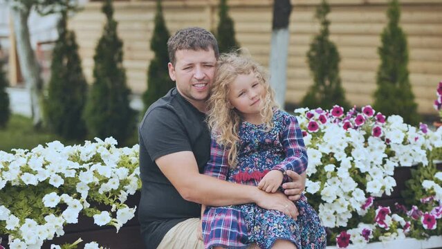 A portrait of a father with his young daughter in the garden against a background of white petunias.