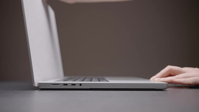 The hand opens the laptop. ACTION. A man opens a laptop with one hand on a gray background. A silver laptop sits on a dark table. Hand lifted the top cover of the netbook