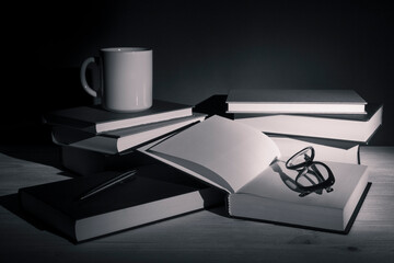 Stack of books with eye-glasses and a cup on a table. Low-key still-life photo, made on studio with...