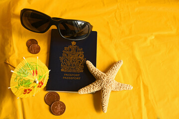 Travel passport with dark sunglasses, cocktail umbrella, starfish and foreign currency on yellow background with copy space.