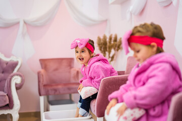 Obraz na płótnie Canvas A little girl in a children's spa. She is sitting in a pink bathrobe with a big bow on her head and waiting her turn for treatment.