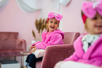 A little girl in a children's spa. She is sitting in a pink bathrobe with a big bow on her head and waiting her turn for treatment.