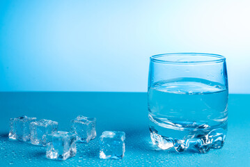 Glass with water and ice cubes nearby