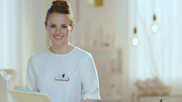 smiling female employee with clipboard in modern beauty studio.