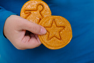 closeup female hand holding round yellow caramel sugar cookies with embossed star for popular Korean children's game, cut out figure with needle, do not crumble pattern, holiday homemade food
