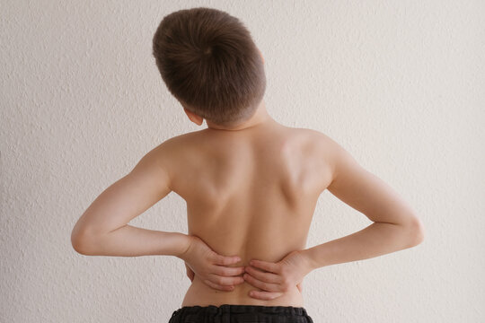 naked back of boy, child 8-10 years old grabbed a sore spot, curved spine, pain in spine, concept of therapeutic massage for osteochondrosis, scoliosis, back pain, intervertebral hernia