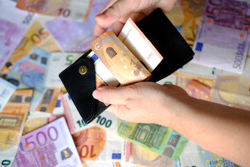 closeup female hands taken out 50 euro banknotes of european union of black wallet against background of scattered paper banknotes on table, concept of payments, savings, banking, cash out currency