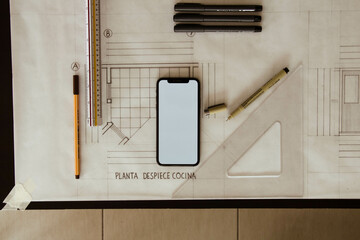 Celular con pantalla en blanco sobre planos arquitectónicos.