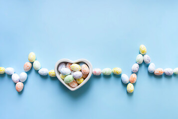 on a blue background, a heart vase with candy eggs and next to it is a cardiogram graph from eggs of different colors