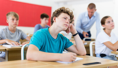 Fototapeta premium Teenager sitting in class room. Male teacher explaining something to them.