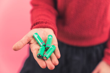 Palm of a caucasian person in a red sweater holding four batteries over pink background. Ecology and recycling concept. High quality photo