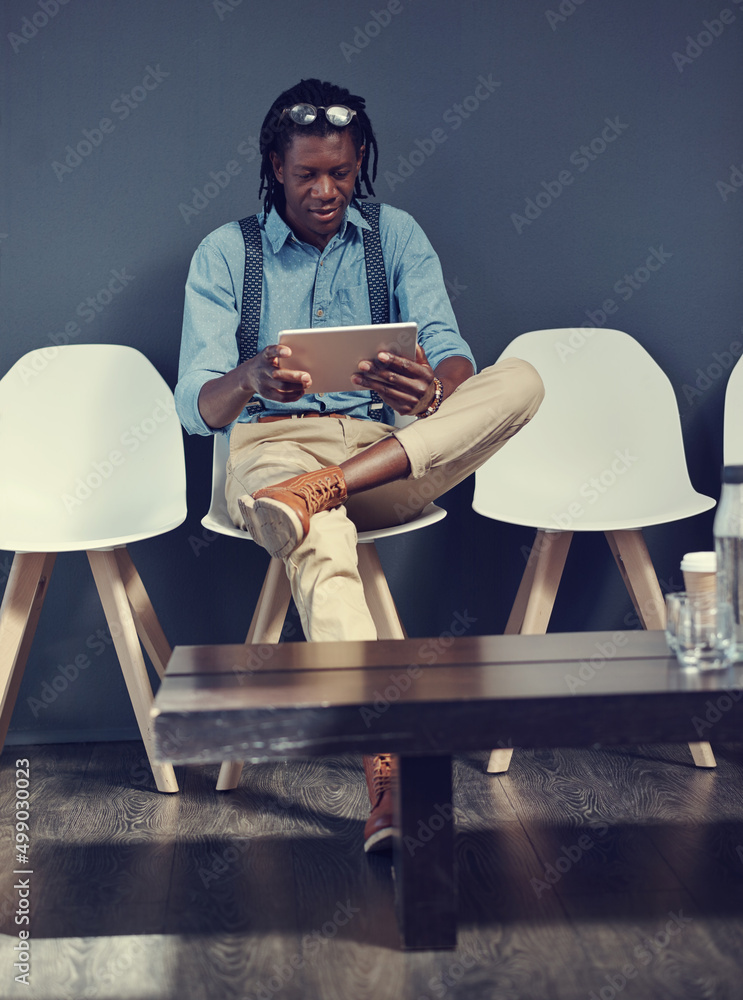 Poster Using this time to catch up on social media. Shot of a young businessman using a tablet while waiting for an interview.