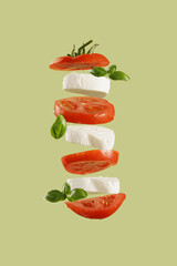 Italian salad caprese: slices tomato, mozzarella, basil leaves on green background flying in the...