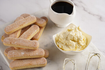 Step by step process of preparing italian dessert tiramisu out of ladyfinger biscuits, mascarpone cheese, espresso on white marble background