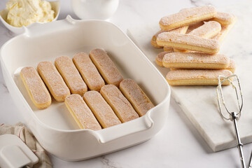 Step by step process of preparing italian dessert tiramisu out of ladyfinger biscuits, mascarpone cheese, espresso on white marble background