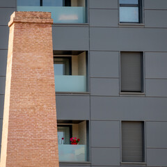 Black facade of a building with a flower pot on a balcony and a brick chimney in front