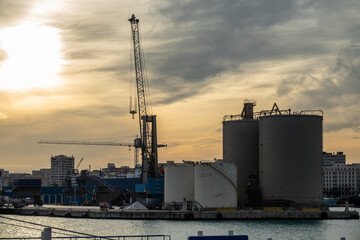 Obraz premium Oil storage tanks and cranes in the harbor at sunset