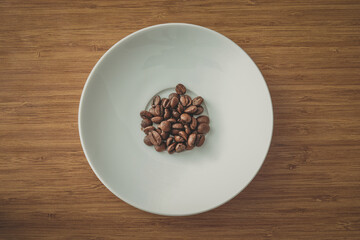 Fresh roasted coffee beans in the coaster on wooden background, selective focus.