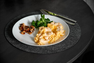 Beautiful breakfast in a white plate on a black table. Omelet with cheese, mushrooms and spinach on a white plate. Eggs with cheese. Beautiful breakfast service. A green napkin lies near the plate.