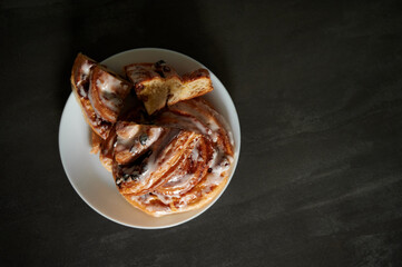 Beautiful serving and serving of cinnabon. Sliced cinnabons on a white plate stand on a black table.