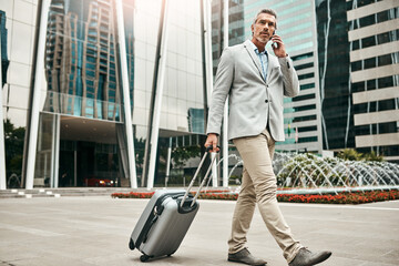 Ive landed and Im ready to talk business. Shot of a mature businessman talking on a cellphone while walking with a suitcase in the city.