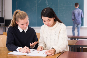 Intelligent girl student helping her Chinese girl schoolmate prepare for exam in classroom