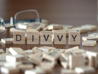 the acronym divvy for dividend word or concept represented by wooden letter tiles on a wooden table with glasses and a book