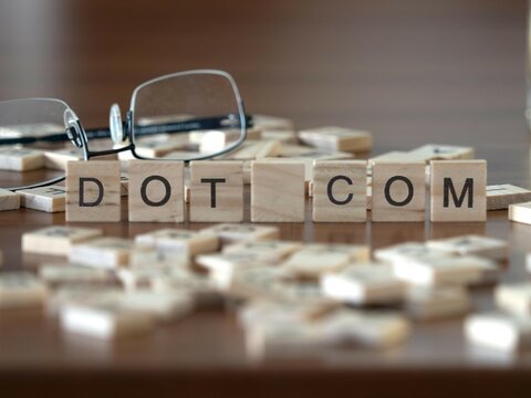 dot com word or concept represented by wooden letter tiles on a wooden table with glasses and a book