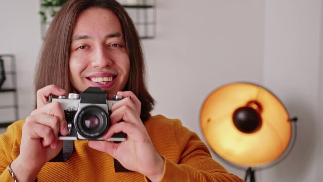Bearded caucasian long-haired freelancer guy taking photos with his camera and looking at camera with a smile on his face. High quality 4k footage