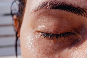 Close-up of closed feminine eye with long eyelashes and eyebrows with water drops