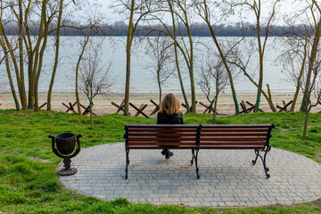 Ukrainian girl sitting on bench and looking at anti-tank hedgehogs on sea shore. Militrary invasion...