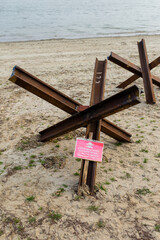 Czech anti tank hedgehoges and warning sign on river bank. Antitank obstacles on sand. Defensive war of Ukraine against Russian agression © aseiryk