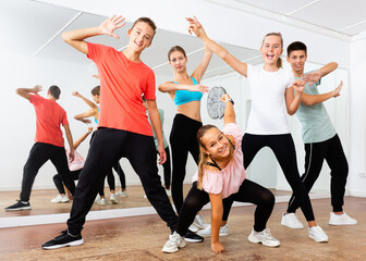 Cheerful happy teenage boys and girls having fun in choreography class, posing with female trainer