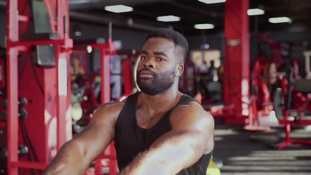African american man bodybuilder with wireless headphones exercising on seated low row machine at gym