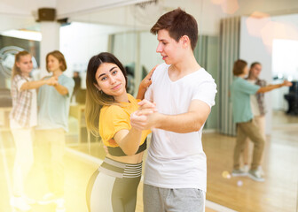 Young girls and boys dancing waltz together in ballroom during group class.