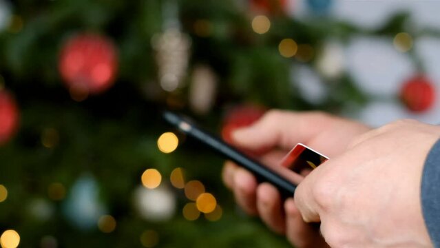 Christmas shopping. Festive online shopping.Credit card and mobile phone in hands on shining Christmas tree background. 4k footage