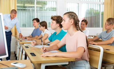 Portrait of focused teenage schoolgirl writing lectures in workbooks in classroom during lesson..