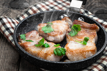 Fried pork slices in frying pan on wooden table