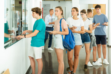 Group of teenage students queuing at front office on college campus, awaiting registration for...