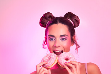 fashion girl gluttonously gobbling up a pair of donuts on a pink background