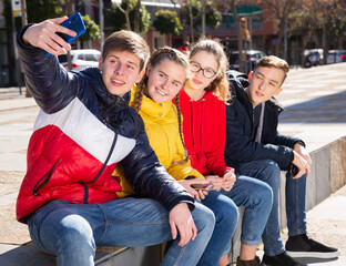 Portrait of four young happy teenagers taking self picture using mobile phone outdoors
