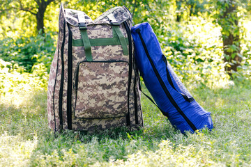 Defocus military backpack and blue tent or sleeping bag. Army bag on green grass background near tree. Military camouflage army rucksack. Tourist summer hiker. Tourism concept. Out of focus