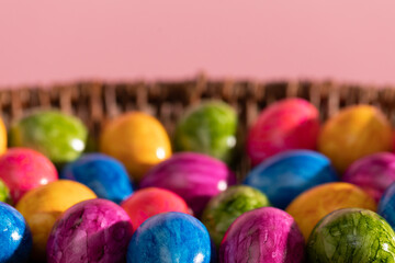 Wicker basket full of colorful Easter eggs on pink solid background. Easter.