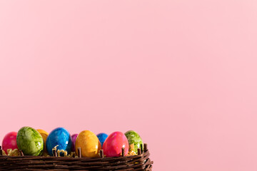 Wicker basket full of colorful Easter eggs on pink solid background. Easter.
