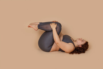Fat ginger woman with obesity oversize, lying in knees to chest pose asana yoga, trying losing...
