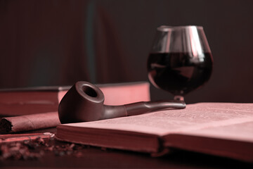 Moody pastel image of the reading cabinet with smoking pipe, brandy and books. Classic vintage relaxation concepts