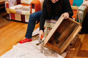 Woman in process of fixing old box made of wood with hammer in workshop for renovation. Giving old...