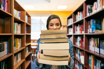Its a stack of knowledge. Portrait of a university student holding a pile of books in the library at campus.